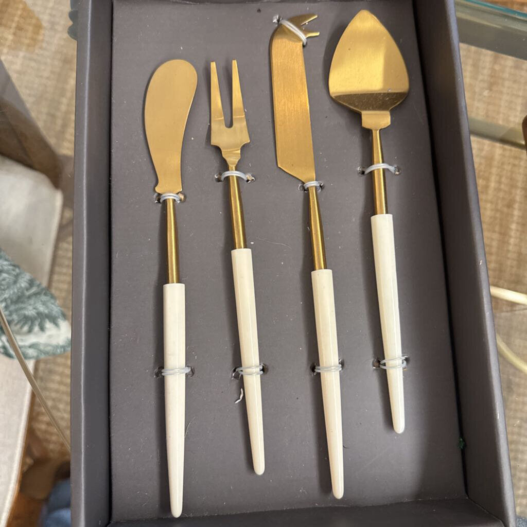 A 4-piece cheese and carving utensil set with gold-tone metal heads and cream-colored handles, displayed inside a dark gray presentation box.